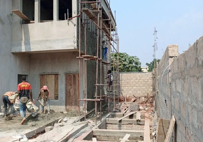 Maçons au travail devant un bâtiment à étage en construction, échafaudage en façade