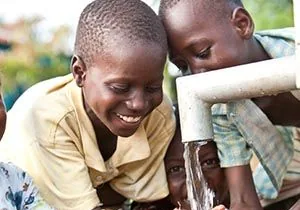 Enfants se rafraîchissant les mains sous l’eau d’une pompe